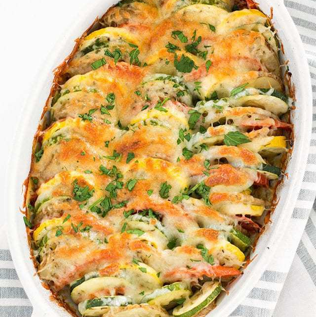oval casserole dish with summer vegetable tian covered in melted cheese and herbs.
