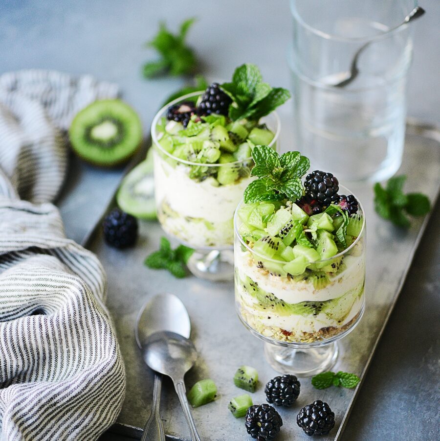 two bottles of kiwi parfait garnished with a mint, fresh cut kiwis and blackberries.