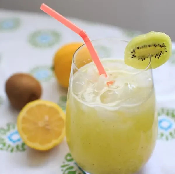glass of kiwi lemonade with a straw and a slice of kiwi on the rim.